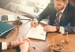 Attorney signing documents at his desk infront of his client How to Advocate for Affordable Medications in Personal Injury Cases